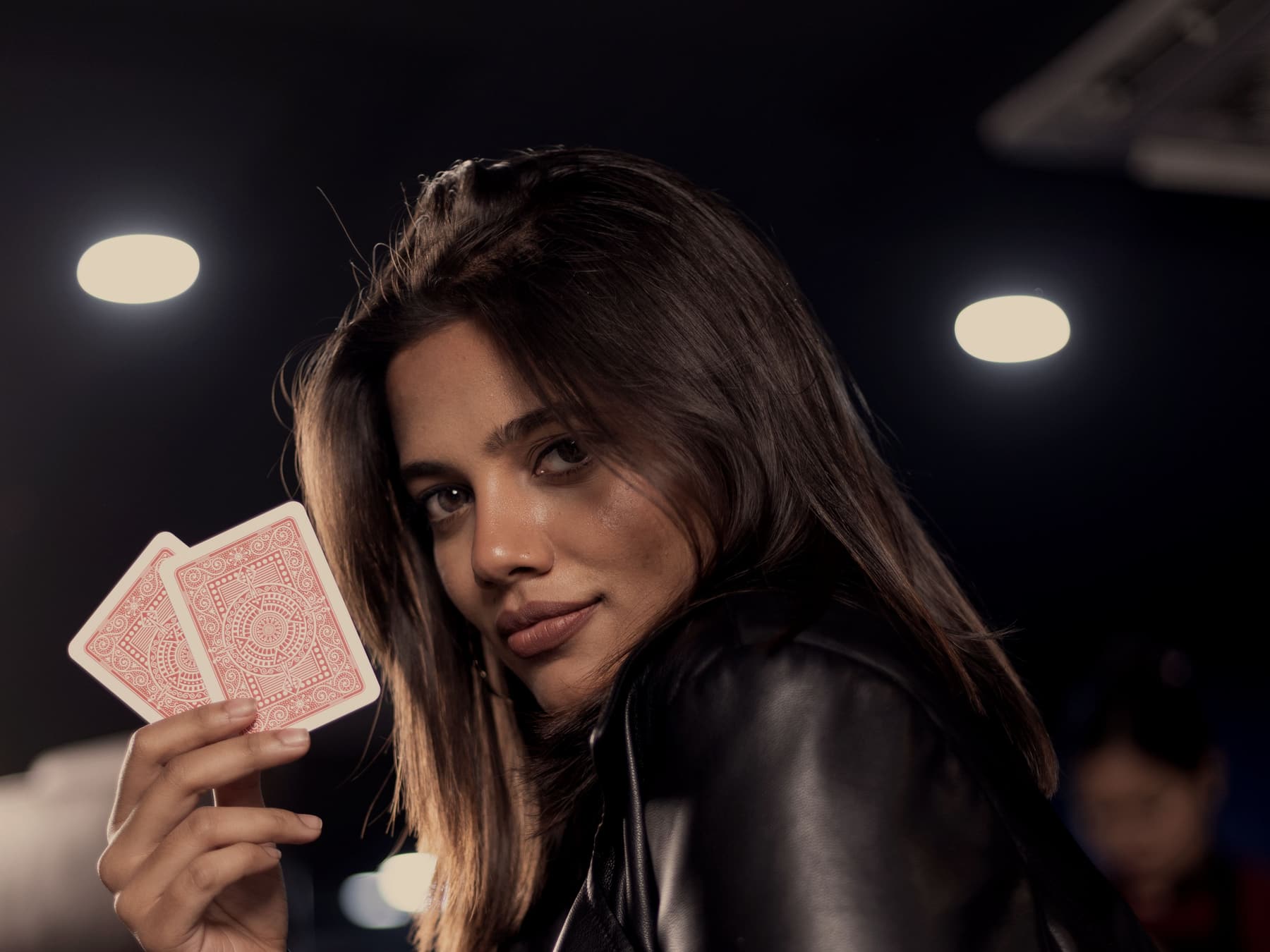 A player holding two cards beneath the room's ceiling downlights, the far side of the room in shadow.